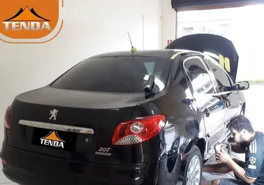Profissional da Tenda trabalhando na lateral de um Peugeot 207 preto dentro da oficina em Maringá